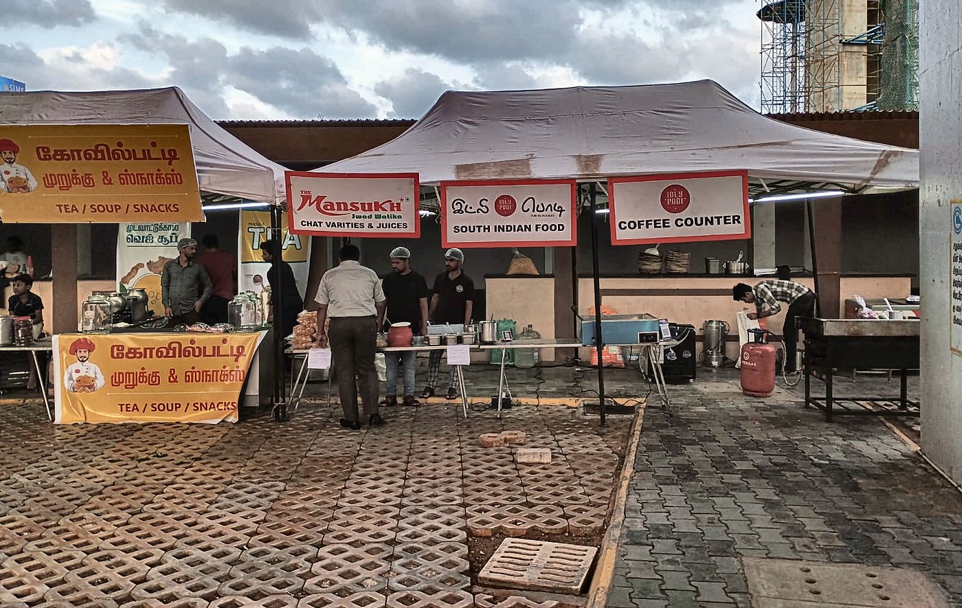 Food stall counters run by Flavours Tec Kitchen, including Mansukh Swaad Watika and Idly Podi, at a live event