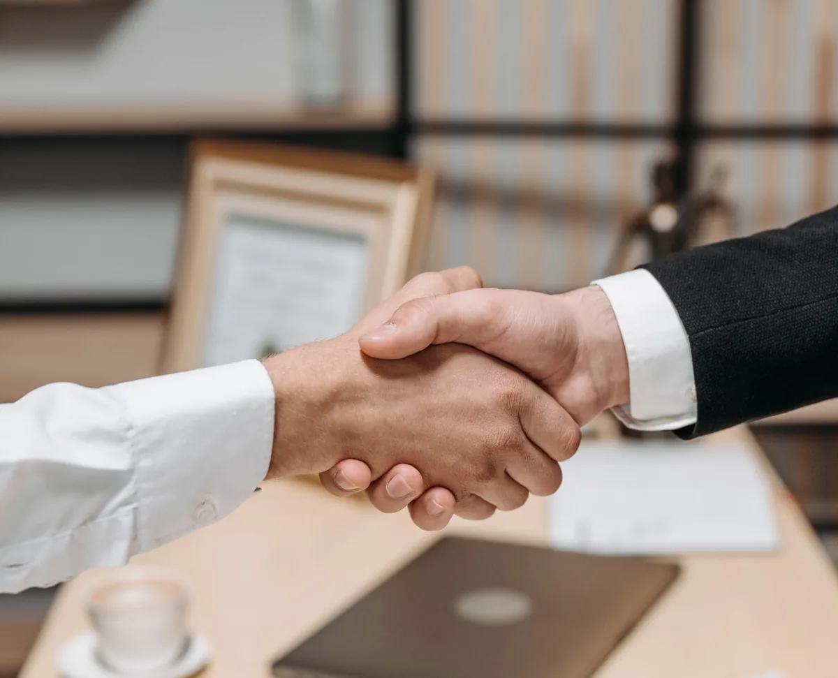 A handshake over a desk with a laptop and documents