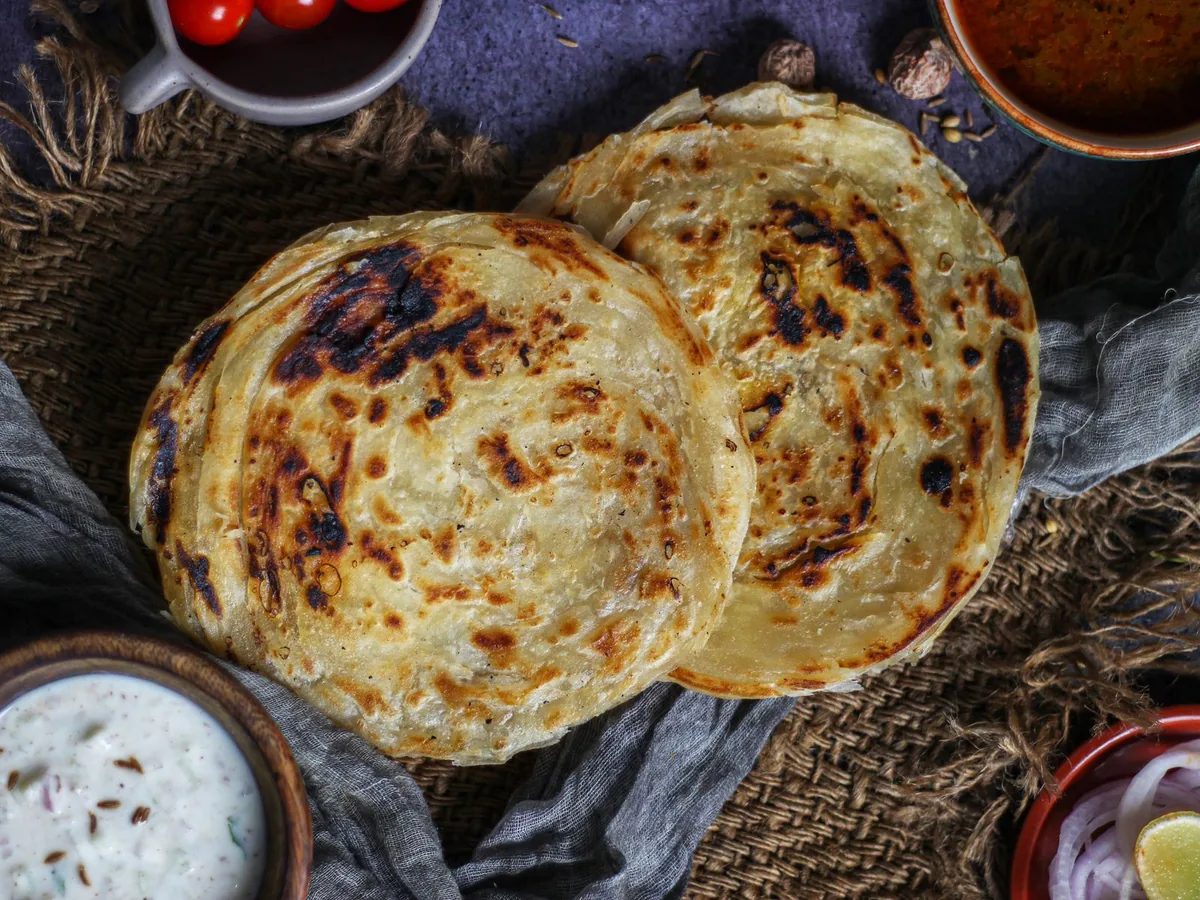 Parotta served with curry, raita and onions